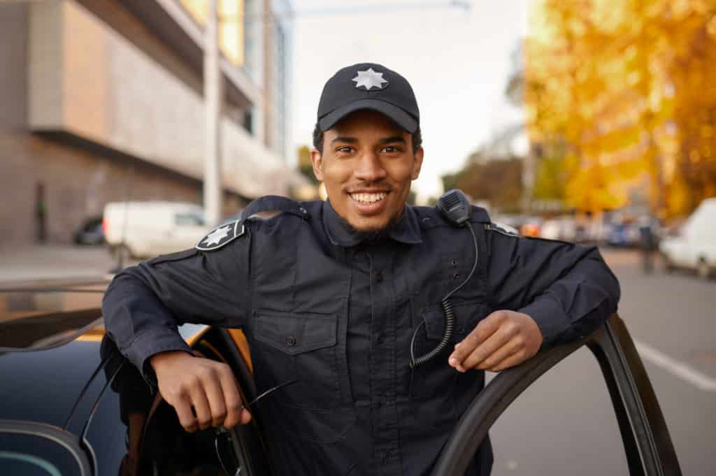 Smiling police officer in uniform poses at the patrol car.